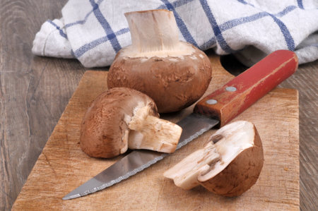 Raw brown button mushrooms on a cutting board with a knifeの写真素材