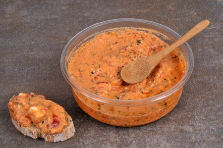Ktipiti in its packaging with a wooden spoon next to a slice of bread on a gray background