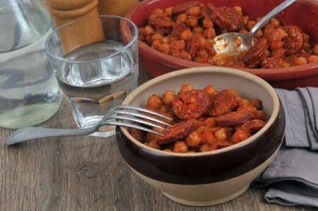 Bowl of chickpeas and chorizo with a fork next to a glass of water served at the tableの写真素材