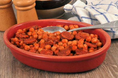 Dish of chickpeas and chorizo with a spoon lying on a tableの写真素材