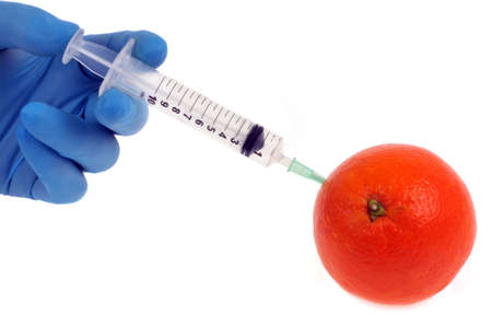 Pesticide concept with a hand injecting a chemical treatment into an orange close-up on a white backgroundの写真素材