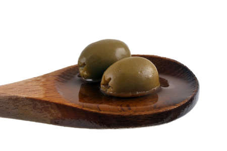 Pitted green olives in olive oil in a wooden spoon close-up on a white backgroundの写真素材