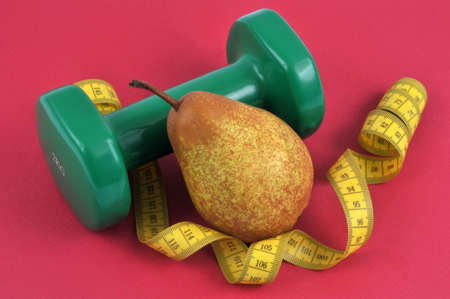 Pear diet concept with flexible meter and dumbbell on red backgroundの写真素材