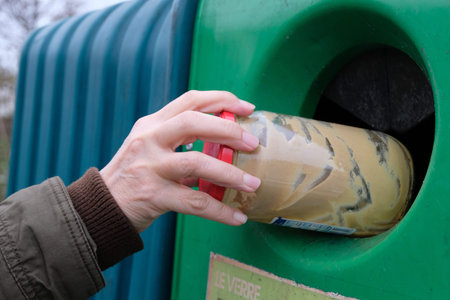 Hand throwing a glass jar into a French recycling bin