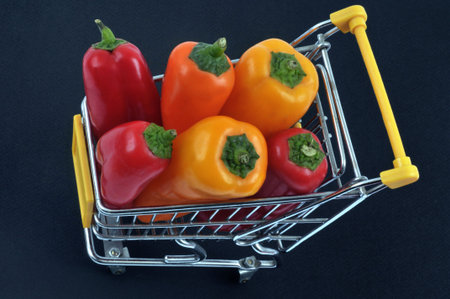 Supermarket trolley full of mini peppers seen from above close up on black background