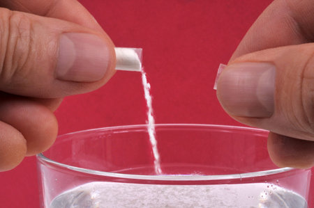 Concept of pouring GHB into a glass with powder from a capsule close-up on a red backgroundの写真素材