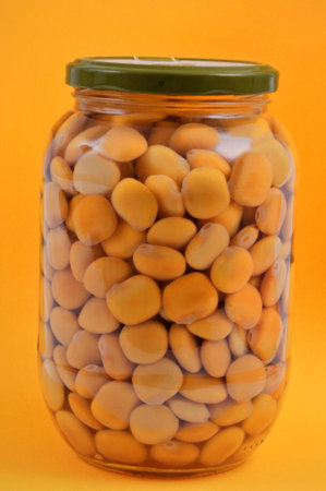 Jar of broad beans close up on yellow background