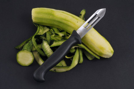 Peeled zucchini with a vegetable peeler on a black background