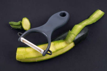 Partly peeled zucchini with a vegetable peeler on a black backgroundの写真素材