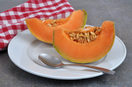 Slices of sliced melon in a plate with a spoon close-up on a gray background
