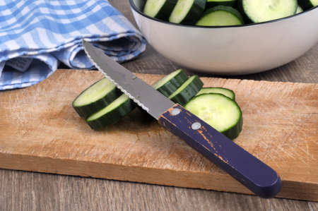 Sliced cucumber with a knife on a cutting board with a salad bowl of cucumber slicesの写真素材