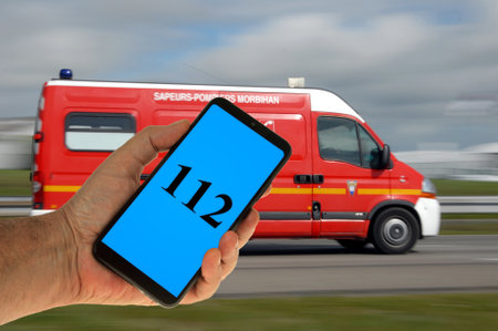Emergency number displayed on a hand held smartphone with a fire brigade ambulance in the backgroundのeditorial素材