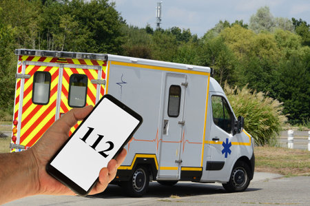 Emergency number displayed on a handheld smartphone with an ambulance in the backgroundのeditorial素材