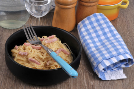 Plate of spaghetti carbonara with a fork served with a glass of waterの写真素材