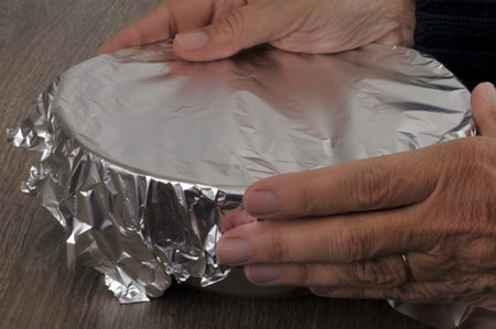 Someone wrapping a bowl of food with aluminum foil close-upの写真素材