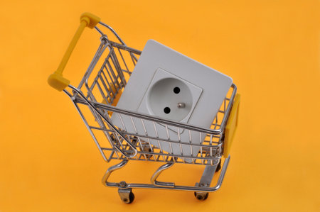 Electricity expense concept with an electrical outlet in a supermarket trolley close up on a yellow backgroundの写真素材