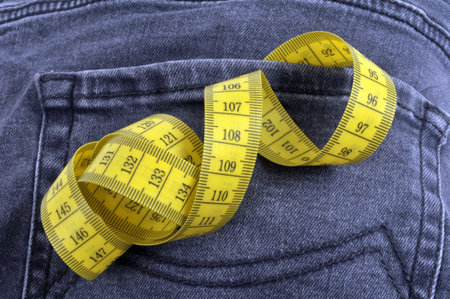 Diet concept with a flexible tape measure sticking out of a jeans pocket close up