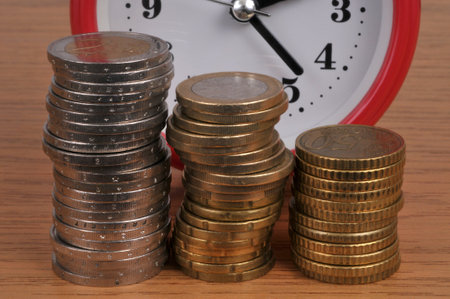 Time is money concept with stacks of eruos coins and an alarm clock in the backgroundの写真素材