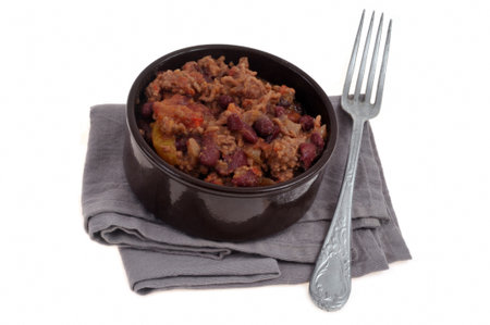 Ramekin of chili con carne on a napkin with a fork close-up on a white backgroundの写真素材
