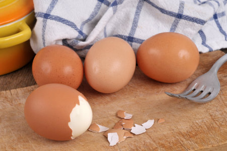 Partly peeled boiled egg close-up with fresh chicken eggs and a fork in the backgroundの写真素材
