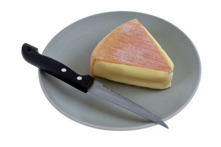 Piece of Saint Nectaire cheese in a plate with a knife close-up on a white backgroundの写真素材