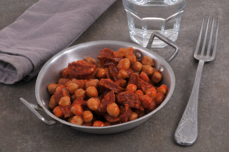 Chickpeas with chorizo in tin dish with fork and glass of waterの写真素材