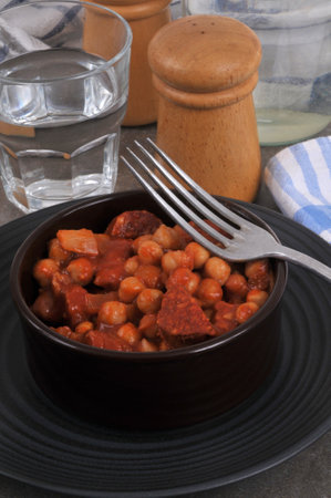 Chickpeas with chorizo served in a ramekin with a fork and a glass of waterの写真素材