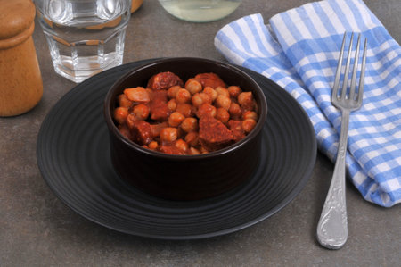 Chickpeas with chorizo served in a ramekin with a fork and a glass of waterの写真素材