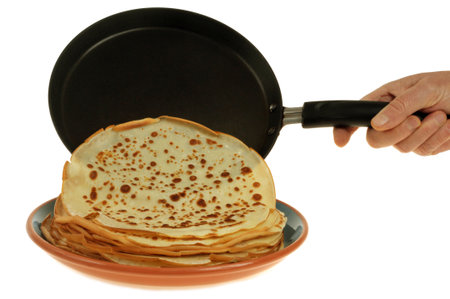 Dragging a crepe from a crepe maker onto a stack of crepes on a plate close-up on a white backgroundの写真素材