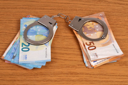 Financial crime concept with handcuffs on wads of euro banknotesの写真素材