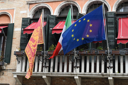 Venetian flag with the flags of Italy and the European Union hanging on a balcony