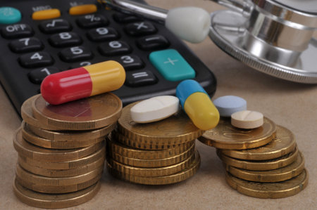 Medicines placed on stacks of euro coins with a stethoscope and calculator blurred in the backgroundの写真素材