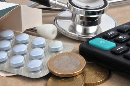 Blister pack of tablets coming out of a box with a stethoscope, calculator and coins closeupの写真素材