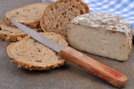 Piece of French cheese Fleur du Maquis with slices of seeded bread and a knife closeup