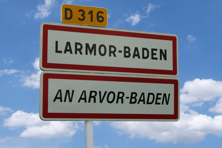 Bilingual sign indicating the town of Larmor-Baden in French and Breton against a blue sky with cloudsの写真素材