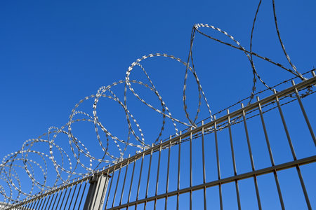 Fence with barbed wire wrapped around it against a blue skyの写真素材