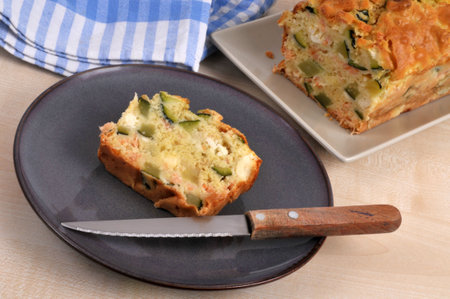 Slice of homemade savory feta and vegetable cake on a plate with a knifeの写真素材