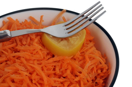 Plate of grated carrots with a fork and a lemon slice close-up on a white backgroundの写真素材