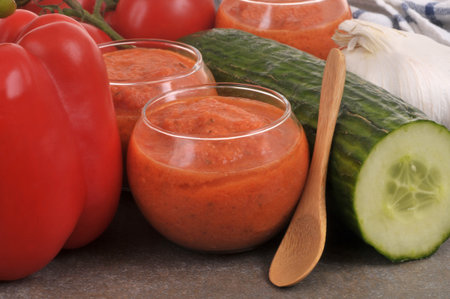 Homemade gazpacho glasses with ingredients and a wooden spoon close-up on backgroundの写真素材