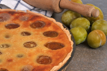 Homemade plum tart in a dish close-up with whole plums and a rolling pinの写真素材