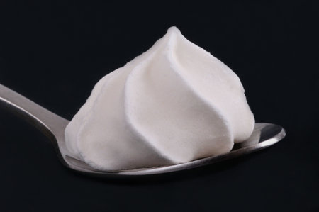 Close-up of a meringue in a spoon isolated on a black backgroundの写真素材