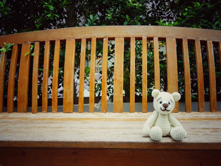 Amigurumi doll bear on bench in park.の素材