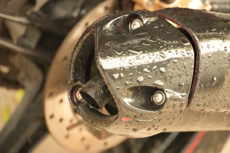 A detailed close-up shows a sleek, black motorcycle exhaust pipe covered in glistening water droplets after rain or wash.の写真素材