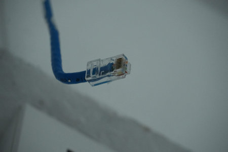 A blue Ethernet cable with a clear plastic connector is shown in a close-up view, with the connector...
