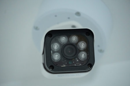 A white security camera with a black lens panel featuring multiple small lenses is mounted on a...