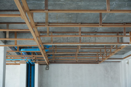 A room under construction with an exposed ceiling featuring a grid of wooden beams and metal...