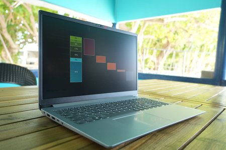 A silver laptop sits on a wooden table, displaying a colorful graph on its screen, with a blurred...