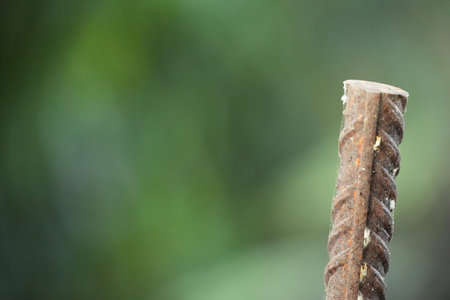 A rusty metal rebar stands vertically with a softly blurred green background.の写真素材