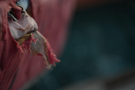 A piece of torn reddish fabric hangs loosely against a dark, out-of-focus background.の写真素材