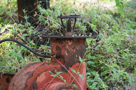 The rusted top of an abandoned red industrial pump features a distinct sprinkler mechanism.